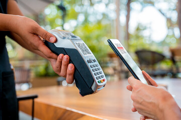 Woman using contactless payment by mobile phone with QR code at cafe