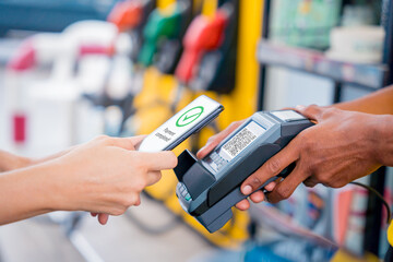 Woman using contactless payment by mobile phone with QR code at car filling station