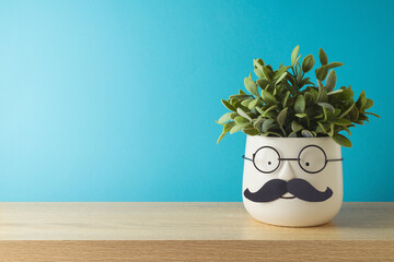 Happy Father's day concept with cute funny plant with mustache and eyeglasses on wooden table over blue background