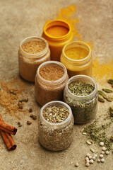 Various colorful spices in small jars on beige concrete background. Side view, close up