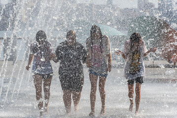 Group sopping girls splashing under jets in pedestrian fountain on hot sunny day. Young womans...