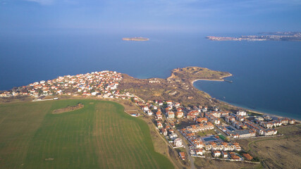 Top view from a drone on a small town with houses, among the field and on the horizon a clear blue sky and sea