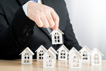 Businessman hand hold for select a home model on the desk in the office, Loan for real estate or saving money for buy a new house to family in the future concept.