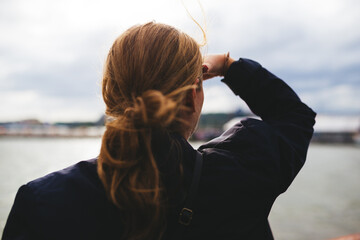The back of a woman watching over out over water with wind in her hair.