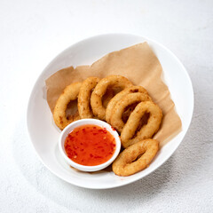 Deep-fried onion rings on paper in white plate. Dish is served with red sauce. Fast food. American cuisine. White background. View from above. Copy space. 