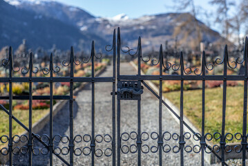 Wrought iron gate at the entrace of a graveyard with the backgound of the snow covered Alps