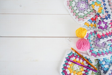 colorful woolen balls with multicolored granny squares and crochet hooks on white wooden ground with space for text - obrazy, fototapety, plakaty