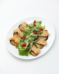 Fried eggplant with lettuce, cherry tomatoes and cheese on white plate. Central Asian cuisine. Vegetarian dish. White background. View from above. 