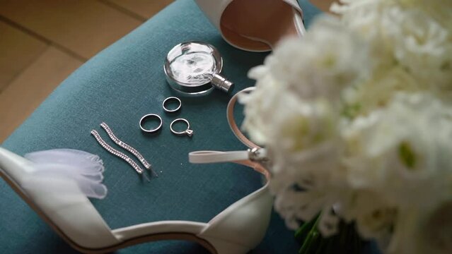 Wedding morning. A bride's bouquet of white flowers, women's high-heeled shoes, jewelry rings and earrings, perfume at blue chair.