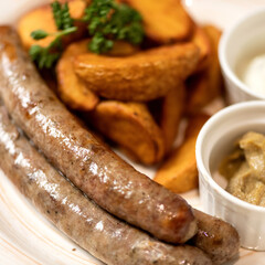 Fried potato wedges and sausages with sauce and mustard on plate. Lunch at restaurant. Fast food. Close-up. 