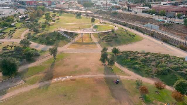 aerial footage of the people relaxing in the park with footpaths, lush green trees and grass, railroad tracks and apartments at Los Angeles State Historic Park in Los Angeles California USA