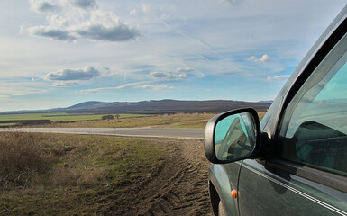 The side mirror of the car and partially the window is a view of the steppe and mountains with a clear sky. The concept of travel and recreation by car