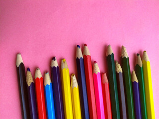 Colored pencils are broken on a pink background. Many different colored pencils. Colored pencil. The pencils are broken. Pencils and a sharpener. Creation. Hobby. Close-up. Copy space. Flat lay.
