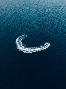 Aerial bird's eye view of jet ski cruising in high speed in turquoise clear water sea
