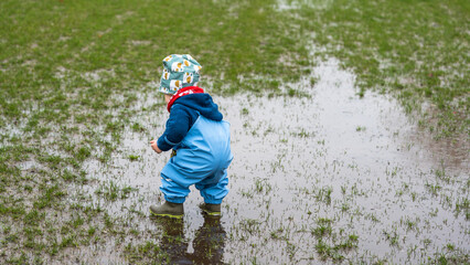 A little child playing in a puddle in a park during rainy weather