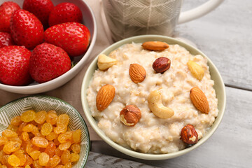 Bowls with tasty oatmeal, nuts, strawberries and raisins on grey wooden background