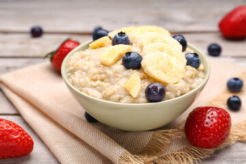 Bowl with tasty oatmeal, blueberries, strawberries and bananas on grey wooden background