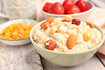 Bowls with tasty oatmeal, nuts, strawberries and raisins on grey wooden background