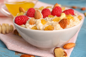 Bowl with tasty oatmeal, raspberries, nuts and raisins on blue wooden background