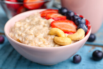 Bowl with tasty oatmeal, strawberries, blueberries and cashew on blue wooden background