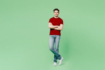 Fototapeta na wymiar Full body smiling happy fun young brunet caucasian man he wears red t-shirt casual clothes hold hands crossed folded isolated on plain pastel light green background studio portrait. Lifestyle concept.