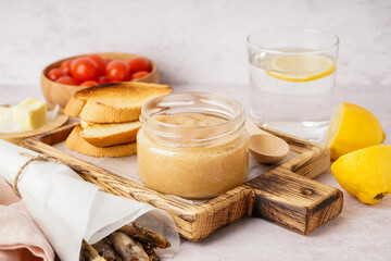 Wooden board with jar of caviar and fried baguette pieces on grey background