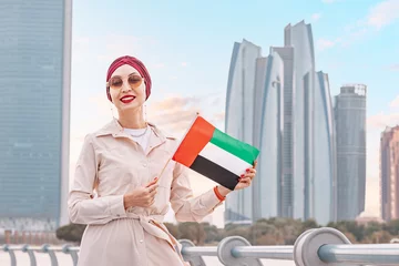 Gordijnen Indian girl with UAE flag against scenic skyscrapers in Abu Dhabi. Immigration, student education and arab emirates citizenship concept © EdNurg