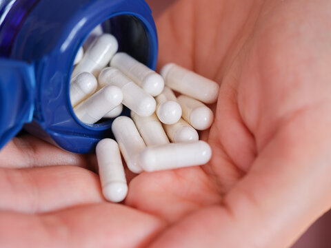 A woman pouring dimethylaminoethanol bitartrate capsules (DMAE) out of a bottle into the palm of her hand
