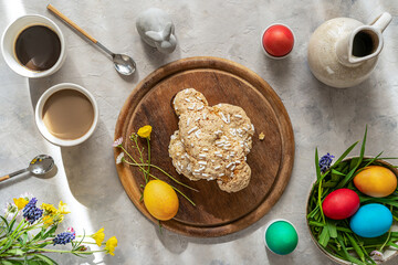 Italian Easter cake Colomba on wooden cutting board with painted eggs, easter decoration, mugs of coffee and wild flowers