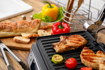 Modern electric grill with tasty steaks and vegetables on table, closeup