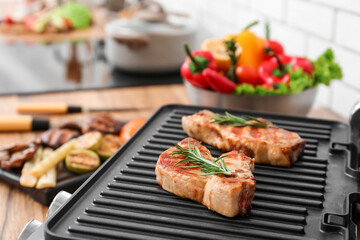 Modern electric grill with tasty steaks on table near light brick wall, closeup