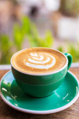 Cup of coffee with latte art on wooden table with morning sunlight through from window. Beautiful morning.