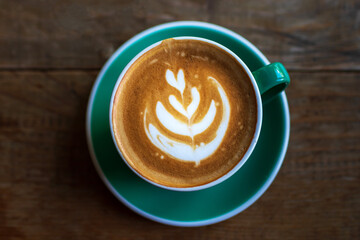 Cup of coffee with latte art on wooden table with morning sunlight through from window. Beautiful morning.