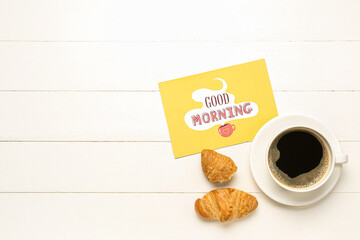 Cup of coffee, tasty croissants and card with text GOOD MORNING on light wooden background