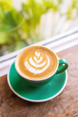Cup of coffee with latte art on wooden table with morning sunlight through from window. Beautiful morning.