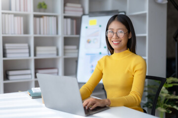 Asian businesswoman sitting using laptop computer at home happily working. Young Asian female student using laptop in library.