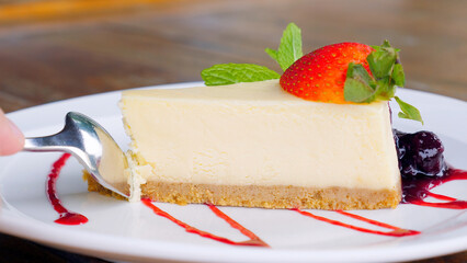 Close-up view of a woman taking bite of a delicious strawberry cheesecake with fresh mint. Tasty New York Cheesecake slice with side of fresh strawberries. Creamy and smooth dessert, gourmet delight.