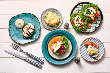 Composition with plates of different eggs Benedict on white wooden table