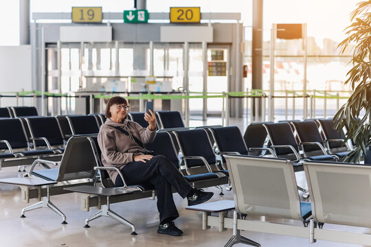 Adult traveler woman sits at airport terminal awaits boarding a flight for departure while uses smartphone with free wi fi. Concept of people sharing informations with new technology while traveling.