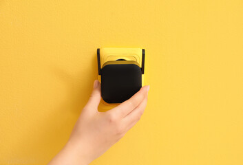 Woman plugging black WiFi repeater in electric socket on yellow wall