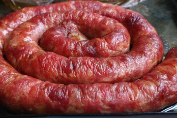 Baked sausage lies on a baking sheet. Juicy and ruddy smoked sausage.