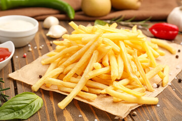 Parchment with tasty french fries on wooden background