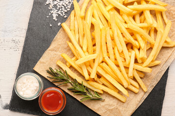 Tasty french fries with sauces and salt on light wooden background