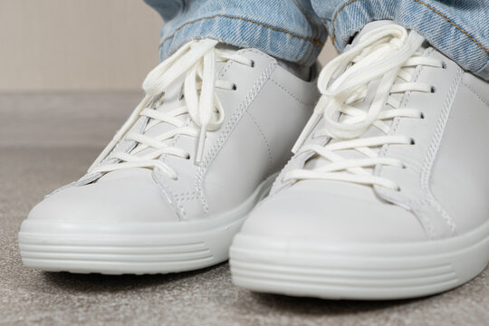 Women's white leather sneakers on the legs indoors. Shoe care. Shoe laces and lacing