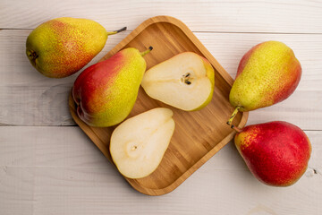 Four whole and two halves of organic sweet pears on a bamboo plate, on a white wooden table, top view.