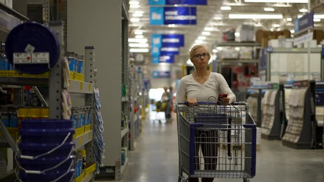 Attractive mature elderly blonde woman pushing shopping cart in hardware store. Concept of older person shopping for home renovation experience