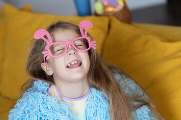 Cute little child girl  in blue fluffy coat wearing bunny ears glasses a on Easter day. Easter girl portrait, funny emotions, surprise..