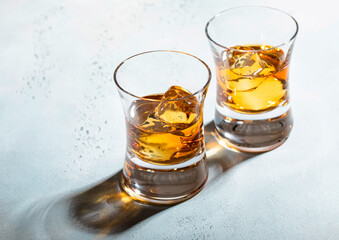 Glasses of whiskey with ice cubes on light background.