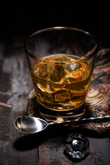 Glass of single malt whiskey with bar spoon and ice cubes on wooden background.