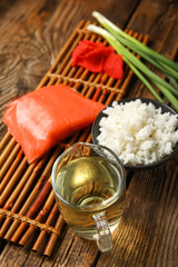 Bamboo mat with vinegar, boiled rice, salmon, ginger and green onion on wooden background, closeup